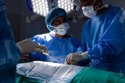 Preview: Diverse female doctors with face masks doing surgery in hospital operating room