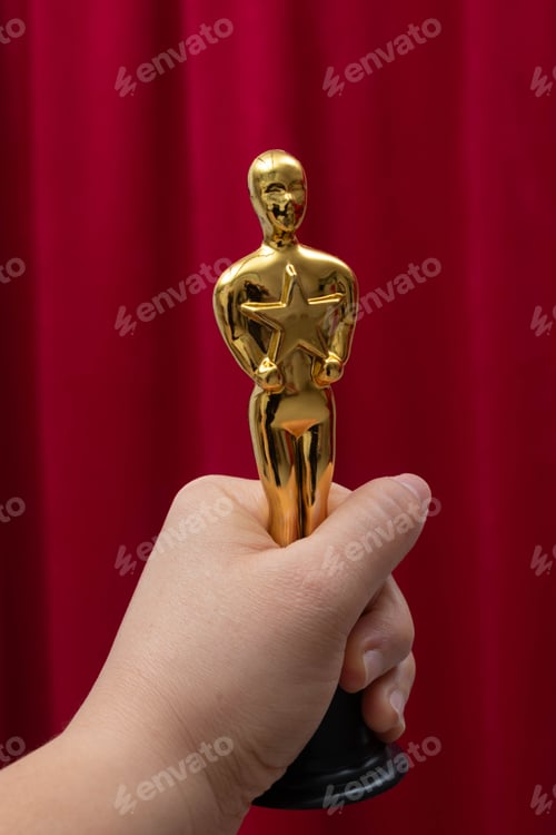 Vorschau: Goldene Preistrophäe in der Hand vor rotem Vorhang