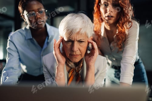 Preview: An old angry businesswoman looking at laptop with her team at office.