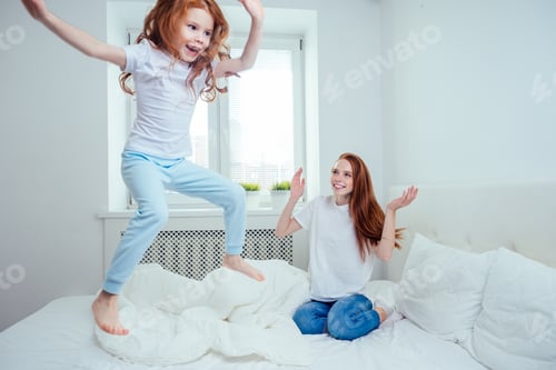 Preview: mom and girl are jumping on the bed at home. success concept
