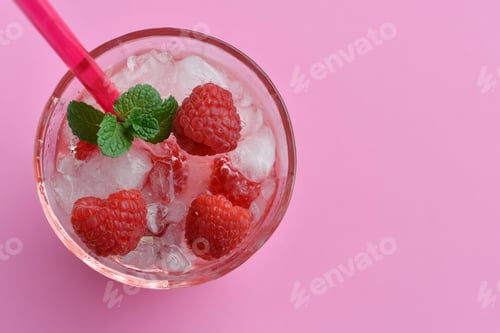 Preview: Colorful pink cocktail drink beverage with raspberries & mint in an icy glass on pink background.