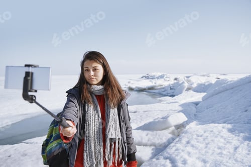 Preview: Female traveler outdoors at icy landscape using monopod to make selfie picture