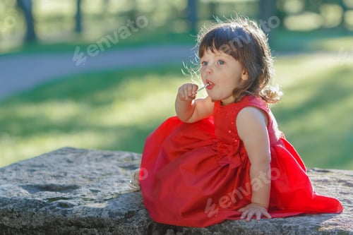 Preview: A little girl in red dress holding lollipop.