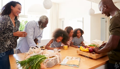 Preview: Grandparents Sitting At Table With Grandchildren Playing Games As Family Prepares Meal
