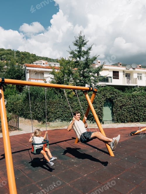 Preview: Dad and little girl swing on chain swings at the playground