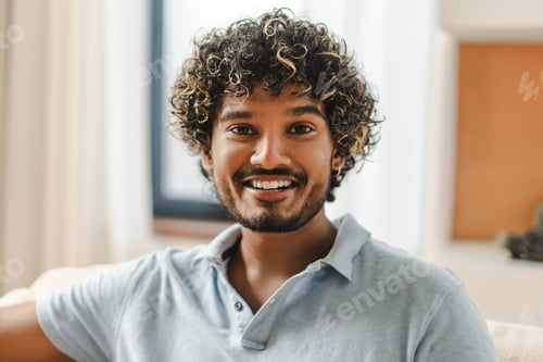 Preview: Portrait of smiling Indian young man with curly hair sitting on sofa at home