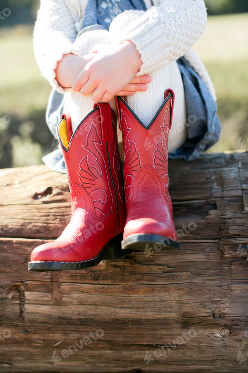 Preview: Neck down view of girl sitting on log wearing red cowboy boots