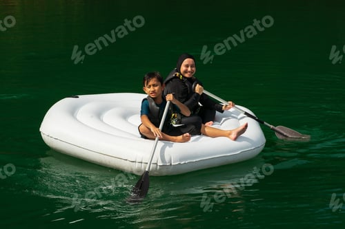 Preview: son and mother in burqini, hijab swimming suit paddling inflatable boat on Lake kenyir, malaysia.