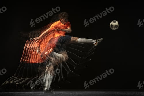 Preview: Young caucasian football soccer player in motion and action in mixed light on dark background