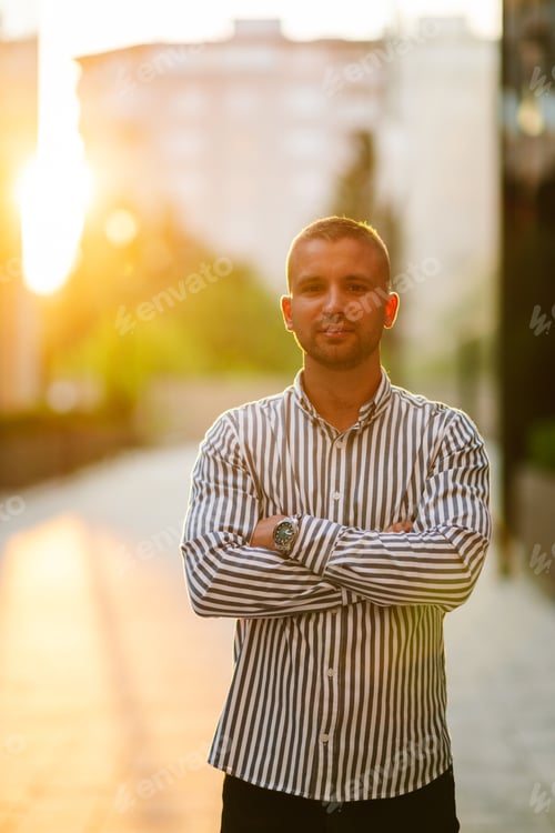 Preview: Confident businessman posing with folded arms at sunset in the city