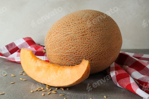 Preview: Ripe melon on gray textured table with kitchen towel