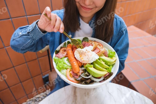 Preview: Closeup image of a young woman holding and eating salad
