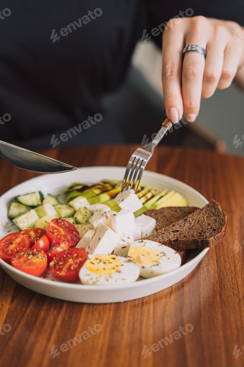 Preview: Girl eats with fork vegetable salad with cheese and eggs and rye bread on white plate