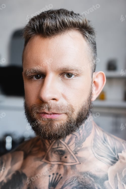 Preview: portrait of bearded, shirtless tattooed man looking at camera