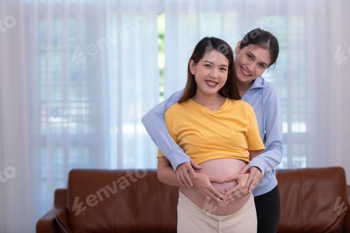 Preview: Happy Asian pregnant woman with yoga teacher teaching pregnancy yoga in her living room.