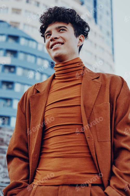 Preview: Young man in stylish brown attire smiling confidently against a modern urban backdrop