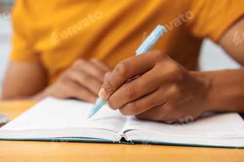 Preview: African American man is holding pen, taking notes while sitting at table, selective focus on hands