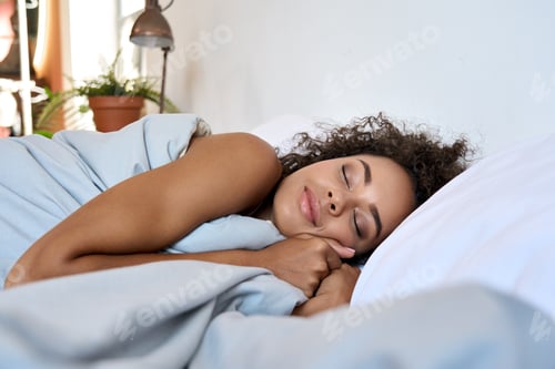 Preview: Young African American woman sleeping in modern bedroom with eyes closed.