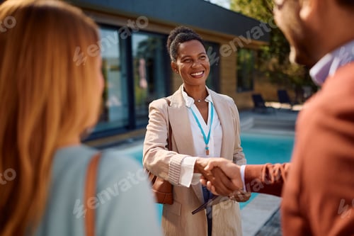 Preview: Happy black real estate agent greeting her clients during open house day.
