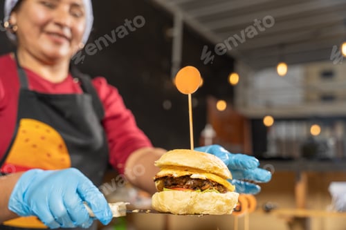 Preview: Cook holding burger with blurred background in kitchen