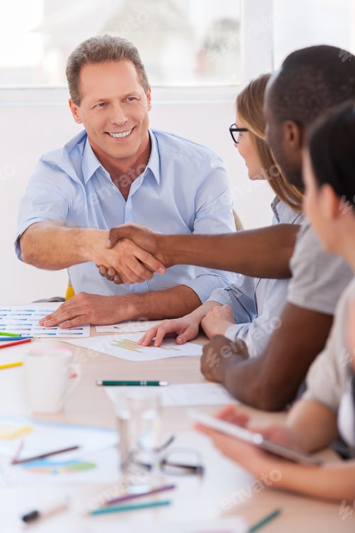 Preview: Welcome on board! Group of business people sitting in a row at the table while two men handshaking