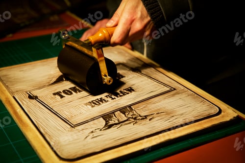 Preview: A signmaker rolling ink across the cut raised surface of linoleum preparing to print.
