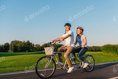 Preview: senior couple riding bicycle together on road in park