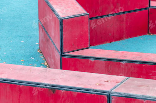 Preview: Blue rubber playground with red bars and fallen leaves: Active outdoor fun among triangular shapes.