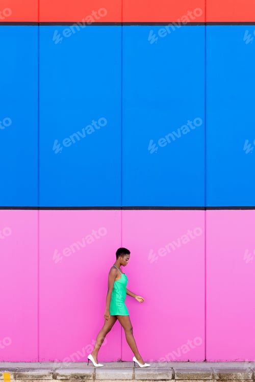 Preview: Stylish young black woman with green dress walking in front of a multicolored background