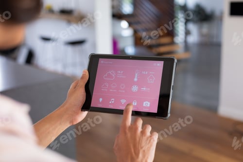 Preview: Hands of biracial man at home using tablet with smart home interface on screen