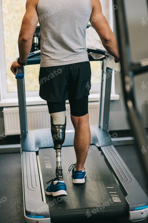 Preview: cropped shot of sportsman with artificial leg walking on treadmill at gym