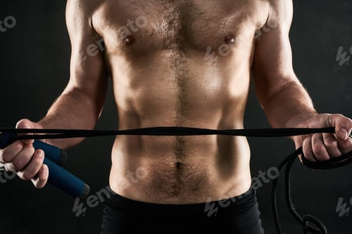 Preview: Studio shot of a mans torso while holding a skilpping rope against a dark background
