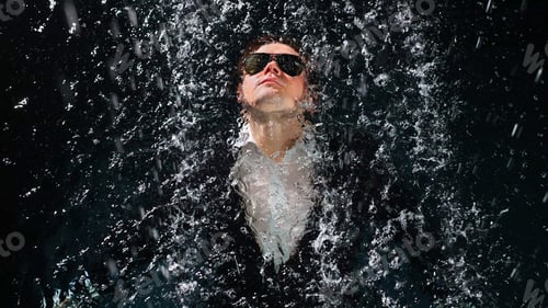 Preview: A man in a suit and sunglasses dives into the water in the rain.