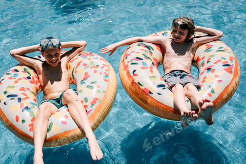 Preview: Two young friends at the pool floating on inflatable donut pool floats on a sunny summer day