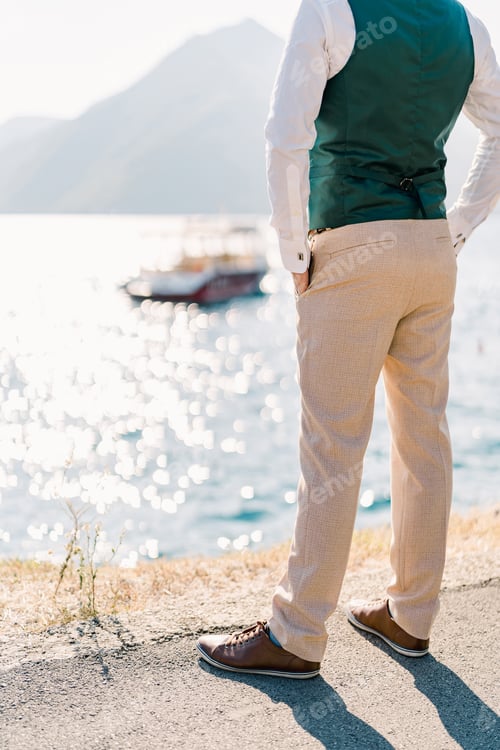 Preview: Man with his hands in his pants pockets stands over the sea. Back view. Cropped