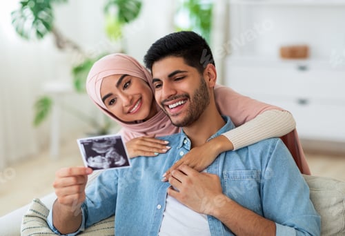Preview: Loving muslim couple with ultrasound photo of their future baby resting at home on sofa, spending