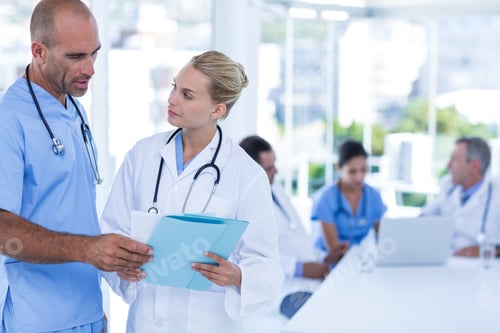 Preview: Two Doctors Looking At Clipboard While Their Colleagues Working In Medical Office