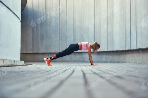 Preview: Strong body. Full-length of young woman with leg prosthesis in sportswear doing plank exercise