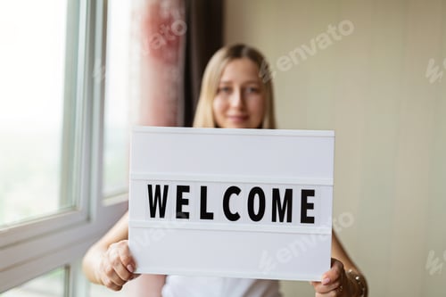 Preview: Young Caucasian woman with blonde hair holding welcoming board