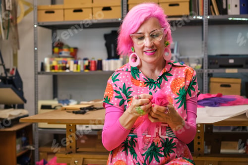 Preview: Seamstress with pink hair and colorfull clothes hand sewing a piece of fabric.