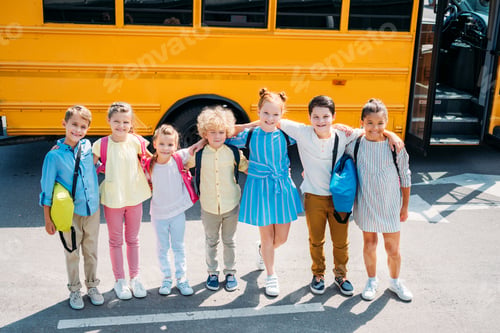 Preview: group of adorable schoolchildren standing in front of school bus and looking at camera