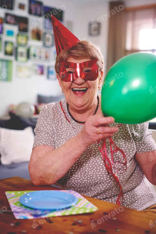 Preview: Senior woman waving balloons at birthday party