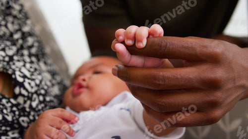 Preview: Close Up Of Baby Son Gripping Father's Finger As He Cuddles Him In Nursery At Home