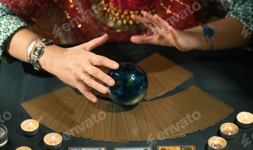 Preview: Tarot reader with tarot cards.Tarot cards face down on table near burning candles and crystal ball.