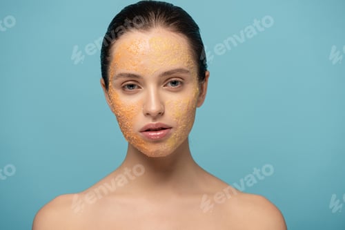 Preview: beautiful girl applying yellow sugar exfoliant on face, isolated on blue