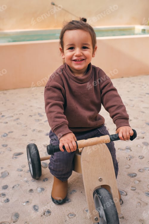 Preview: Content girl on wooden bicycle in daytime
