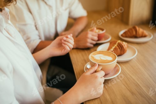 Preview: Happy couple in love drinking hot coffee with croissants, sitting in coffeehouse