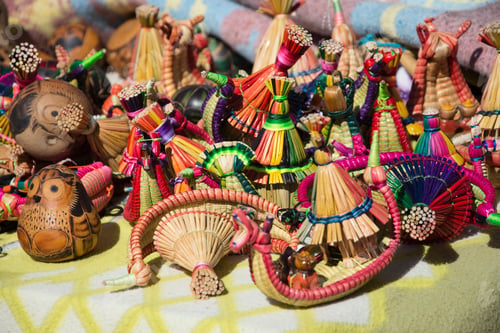 Preview: A close up view of a variety of vibrant handmade small boats made of reeds on a table outdoors