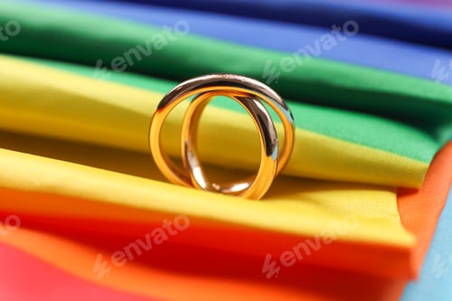 Preview: Rainbow LGBT flag and wedding rings on light blue background, closeup