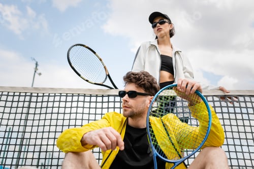 Preview: active lifestyle, couple in sunglasses posing near tennis net, holding rackets, active wear fashion